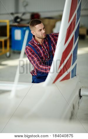 Airplane service crew working on preflight maintenance: Portrait of young mechanic inspecting fuselage of jet plane in hangar