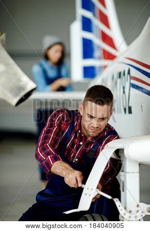 Airplane service crew working on preflight maintenance: strained young mechanic tightening screws in chassis of jet plane
