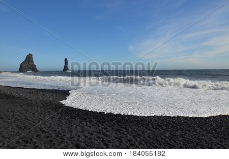 White waves crashing on the shore of Reynisfjara black sand beach with sea stacks.