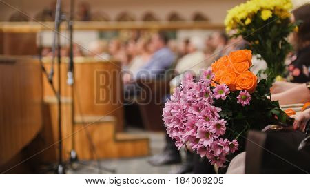 Audience in the concert hall holding flowers for artists on stage telephoto
