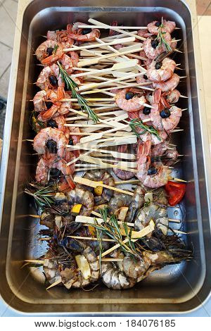 A lot of seafood on skewers grilled shrimp in a metal container. Preparation for a banquet