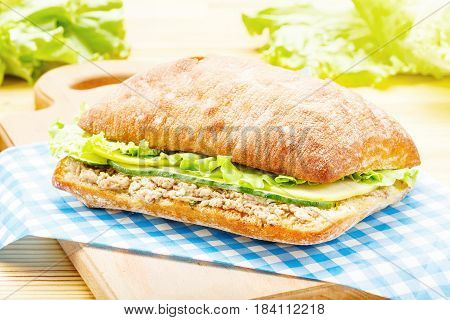 Large ciabatta sandwich with tuna, green, apple and cucumber lying on a blue napkin and a wooden board