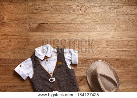 Top view photo of the boy's clothes on the wooden background. White shirt with print, brown vest, bowtie and hat. Cute clothes for little boys. Concept of the children's fashion. Spring or summer children's clothes.