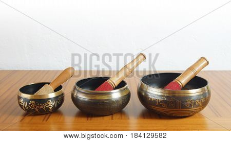 Three Tibetan bowls on a wooden table with white wall background