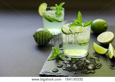 Cold cocktail with lemon liqueur, lime, tonic, ice in two glasses or mojito cocktail on dark background, copy space. Horizontal. Close-up.