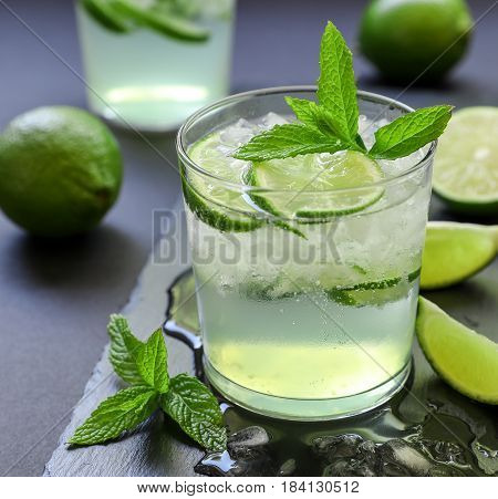 Cold cocktail with lemon liqueur, lime, tonic, ice in two glasses or mojito cocktail on dark background. Close-up.
