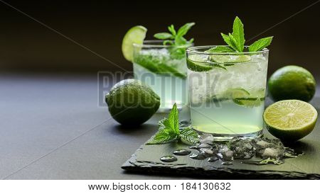 Cold cocktail with lemon liqueur, lime, tonic, ice in two glasses or mojito cocktail on dark background, copy space. Horizontal. Close-up.