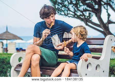 Father And Son Eat Fried Sweet Potatoes In The Park. Junk Food Concept