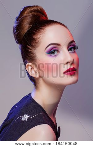 Beautiful young woman with hairdo and bright purple tone make-up. Doll style. Beauty shot on grey background. Copy space.