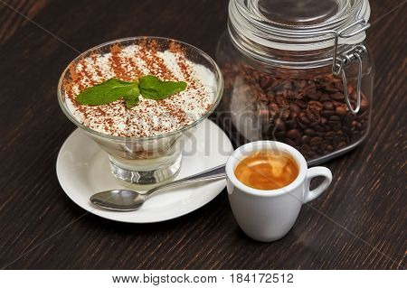Tiramisu creme cake dessert in glass with mint leaves and coffee cup on black wooden background
