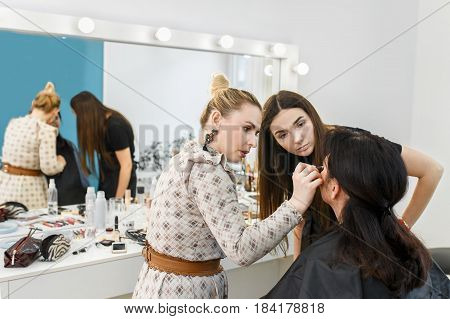 Makeup lesson at beauty school. Professional makeup artist conducts a master class. Make-up artist work in her studio. Real people. Visagiste applying makeup