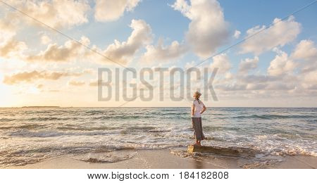 Relaxed woman enjoying sun, freedom and life an beautiful beach in sunset. Young lady feeling free, relaxed and happy. Concept of vacations, freedom, happiness, enjoyment and well being.