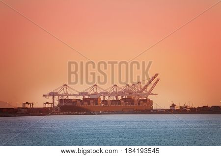 Crane bridge loading containers on barge at Long Beach shipping port at dusk, California, USA