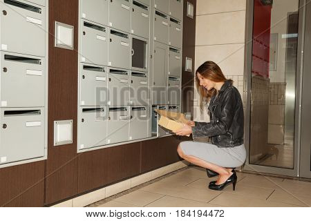 Young woman taking correspondence from mailbox sitting on her hunkers at doorstep