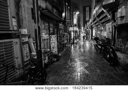 TOKYO, JAPAN - APRIL 8, 2017 - Black and white of a man with an umbrella walking down a lonely alleyway on a rainy night in Tokyo City