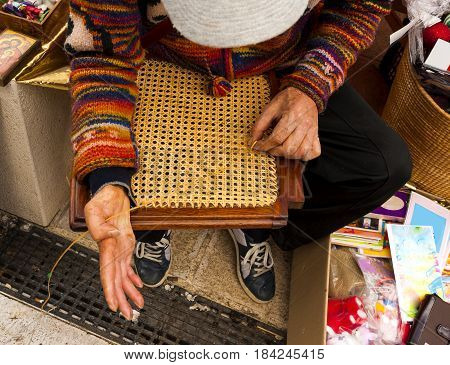 hands of a mender of chairs while repairing an old wooden chair
