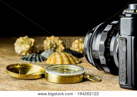 Old fotocamera with sea shells and compass on the brown wooden background
