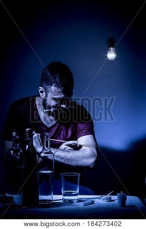 Young man with beard lost in the vices of alcoholism smoking and drug addiction