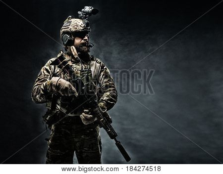Bearded soldier in Combat Uniforms with weapon, plate carrier and combat helmet are on. Studio shot, dark background
