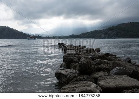 Stone pier on Phaselis bay. Overcast sky with sun rays. Drammatic scene. Located place: Kemer, Turkey.
