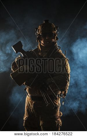 Army soldier in Combat Uniforms with machine gun, plate carrier and combat helmet are on. Studio contour silhouette shot, backlight, dark glowing smoke background