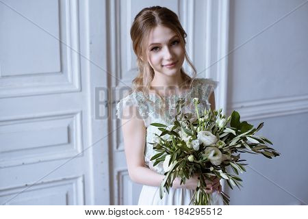 Beauty bride in bridal gown with bouquet indoors. Beautiful model girl in a white wedding dress. Female portrait of cute lady. Woman with hairstyle