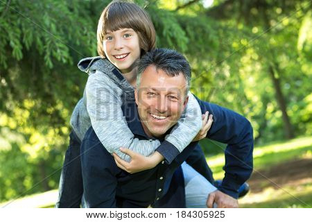 Portrait of father with his son having fun in summer park. Piggyback. Family fun. Happy boy playing with dad summer nature outdoor. Family leisure