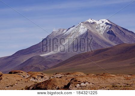 Purple Mountain Landscape, actually an active Volcano, with blue skies and lava rock in foreground