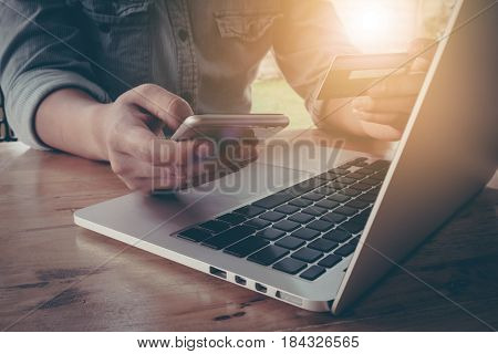 Online paymentMan's hands holding a credit card and using smart phone for online shopping with vintage filter effect