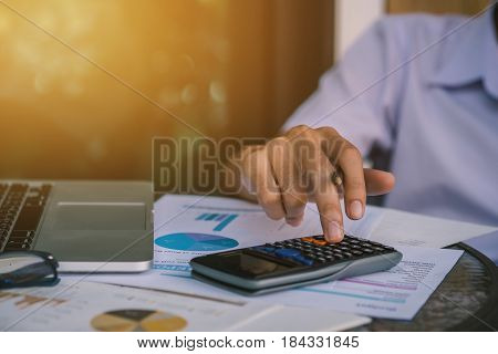 financeaccountingBusinessman analyzing investment charts with calculator laptop calculate technology in officebusiness conceptselective focusvintage color