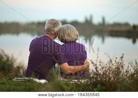 Happy senior couple sitting in summer near lake during sunset