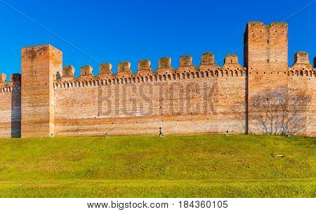 Brick wall and two watch towers in the city of Cittadella, it's a walled city in the province of Padua (Padova), Italy. Man walking on grass along the wall around the old town center