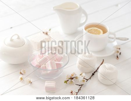 Pastel tea set with zefir and sweets, marshmellow and milk on side, decorated with flowers
