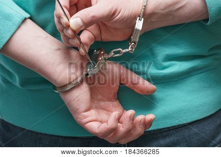 A criminal with hands bihind trying to open handcuffs with piece of wire.