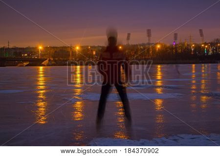 Back blurred view of young man standing on ice at night with city lights in background