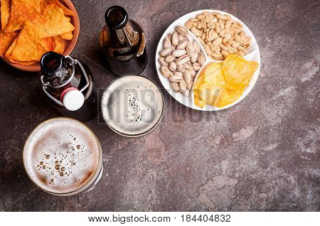 Beer in bottles and glasses on the concrete table. Beer and snacks are pistachio nuts chips and nachos top view. Copy space. Drink and snack for the football match or party