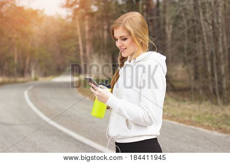 Outdoor Messaging. Portrait Of Young And Beautiful Redhaired Sports Girl Using Her Phone And Keeping