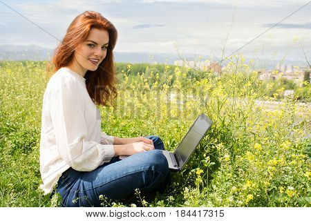Young Successful Redhead Woman Blogger Sittingon The Grass, Writing A New Post For Her Blog ,using N