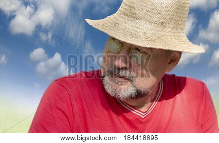 A man with a beard, in a golden pince-nez of the 19th century, wearing a straw hat on the blue of the blue sky