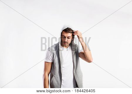 Handsome hipster fitness man in white t-hirt and gray vest with hood. Studio shot on gray background.