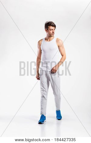 Handsome hipster fitness man in white tank top shirt and gray sweatpants. Studio shot on gray background.