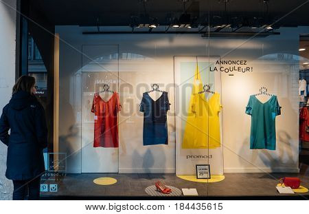 STRASBOURG, FRANCE - APR 27, 2017: young female woman customer admiring the Promod fashion clothing store with multi colored dresses in the vitrines illuminated by spotlight