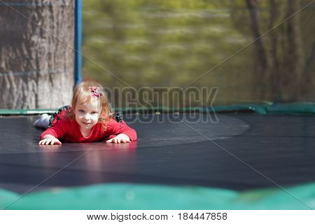 Little Girl In A Red Dress Jumping On A Trampoline In The Park
