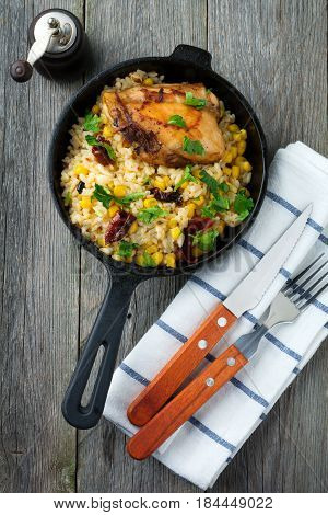 Rice with corn soy sauce and fried chicken thigh on a cast-iron frying pan. Top view. Selective focus.