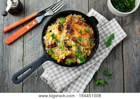 Rice with corn soy sauce and fried chicken thigh on a cast-iron frying pan. Top view. Selective focus.