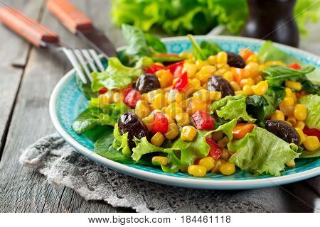 A warm salad with corn pepper olives and lettuce on a blue ceramic plate on a dark background. Selective focus.