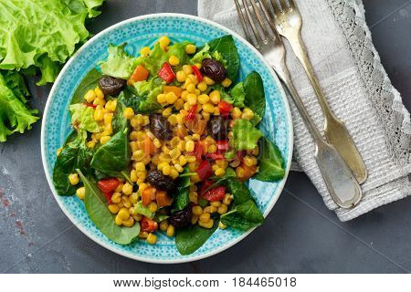 Warm salad with corn pepper olives and lettuce on a blue ceramic plate on a dark background. Selective focus.Top view.