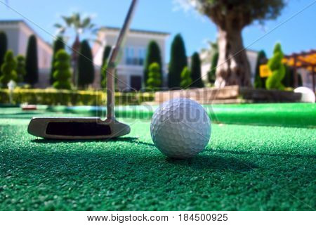 Mini golf scene with ball and club. Sunny day at resort park