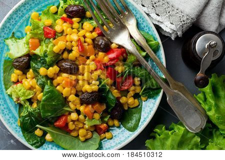 Warm salad with corn pepper olives and lettuce on a blue ceramic plate on a dark background. Selective focus.Top view.