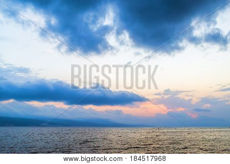 Beautiful morning seascape. Sky with cumulus clouds and a calm sea. Mountains on the horizon. Dawn above the sea.